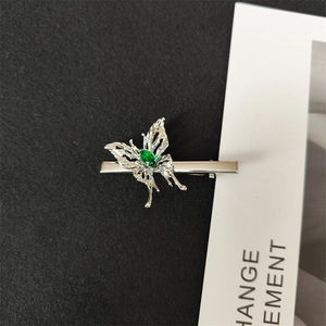 Macro shot of silver hollow butterfly clip with emerald green gemstone on dark backdrop