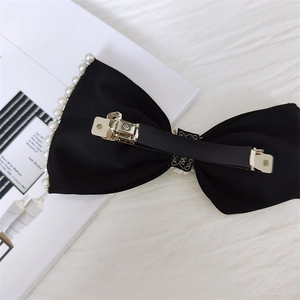 Dettaglio del retro di un fiocco per capelli in raso nero con perle e fermaglio in metallo