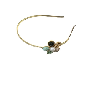 Eleganter Gold-Haarreif mit Strassblumen und einer weißen Perle auf weißem Hintergrund