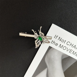 Detail of silver butterfly hair clip featuring a wavy texture and olive green gemstone