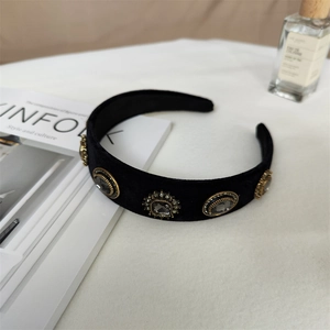 Détail d'un serre-tête baroque en velours noir avec cristaux dorés sur fond blanc Kinfolk
