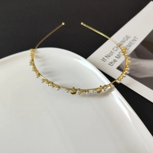 Detail of elegant gold alloy headband with white pearls and leaf accents on ceramic plate