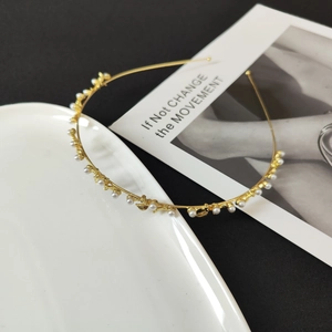 Detail of a thin gold metal headband featuring white pearls and small golden leaf elements