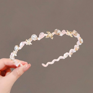 Cerchietto rosa ondulato con cristalli perle e stelle dorate tenuto in mano
