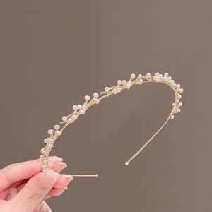 Dettaglio di elegante cerchietto in metallo dorato con delicate perle bianche a ramo
