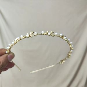 Detailed close-up of a gold pearl headband with small metal leaves held by hand