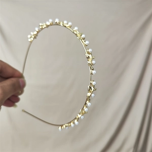 Detail view of a slim gold headband featuring elegant metal leaves and white pearls