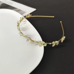 Elegant gold metal floral headband with pearls and green leaf beads on ceramic plate
