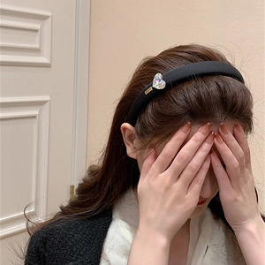 Détail d'un serre-tête en velours noir avec strass en cœur et breloque dorée