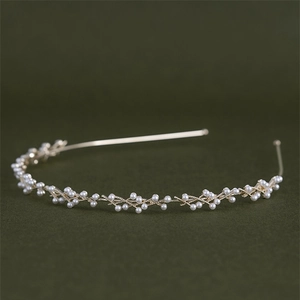 Dettaglio di un elegante cerchietto in metallo dorato con perle bianche su sfondo scuro