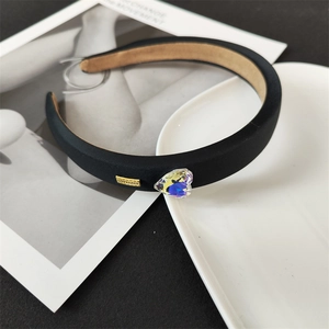 Détail d'un serre-tête noir rembourré avec strass en cœur et plaque en métal doré
