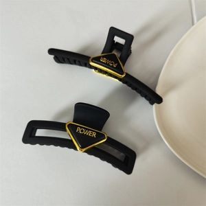Detail of matte black shark hair clips with golden triangular POWER logo insert