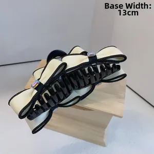 Detail view of a 13cm oversized cream bow hair claw clip with black trim and colorful rhinestones