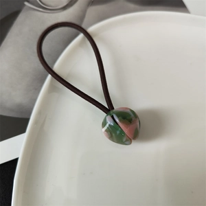 Macro shot of high-elasticity hair tie with green and pink marble texture beads on white plate