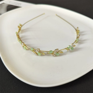 Detail view of a gold-plated flower headband with green leaf charms and white pearls on a tray