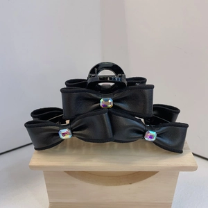 Detail of a black leather bow hair claw clip with colorful rhinestones on wood