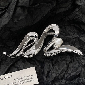 Detail of silver wavy claw clip with pearl on dark textured paper background