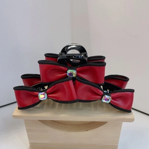 Detail of red faux leather bow hair claw clip with rhinestones on a wooden stand