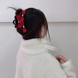 Detailed view of a red satin bow hair claw clip with rhinestones worn on hair