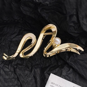 Detail view of a golden wave hair claw clip featuring a white pearl against a black background