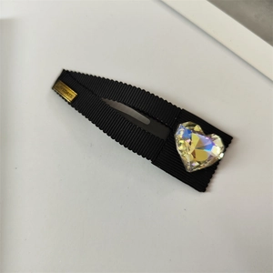 Détail d'une pince BB en tissu noir avec un grand cristal en cœur et une plaque dorée