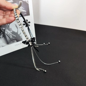 Dettaglio di un cerchietto nero con strass lucidi, farfalla e nappe metalliche sottili