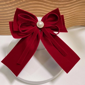 Elegant red velvet bow hair clip with faux pearl and rhinestone center on white platform