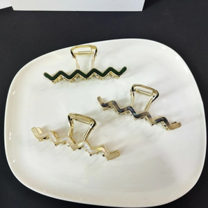 Close-up of wavy acetate hair claws in dark green and marble grey on a white ceramic tray
