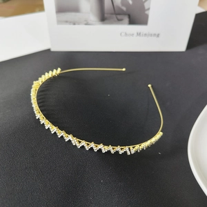 Detail of thin gold metal headband with zigzag rhinestone design on black leather surface