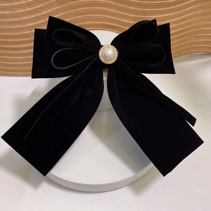 Elegant black velvet bow hair clip with faux pearl and rhinestone center on wooden base