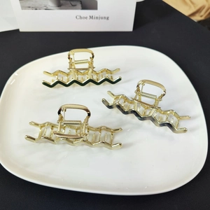 Close-up of three gold wave hair claws with green and beige enamel in a ceramic bowl
