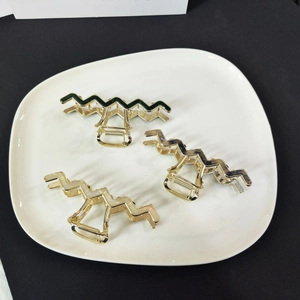 Detailed macro view of three wavy metal hair claws with colorful acetate inlays in a tray