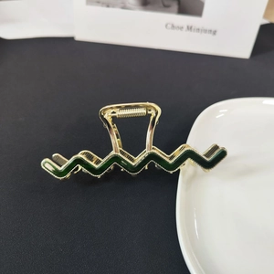 Elegant gold metal wave hair claw clip with dark green enamel finish on black background