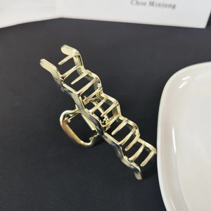 Detail view of the wave-shaped golden metal hair claw clip with geometric hollow design