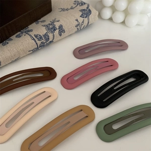 Detail von matten Morandi-Haarklammern in Tropfenform auf floralem Stoffhintergrund