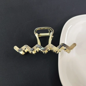 Close-up of golden wave hair claw with marble acetate inlays on white ceramic plate
