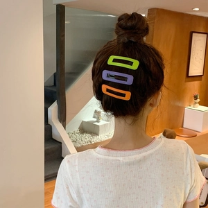 Trois barrettes rectangulaires aux couleurs acidulées portées sur une coiffure de femme