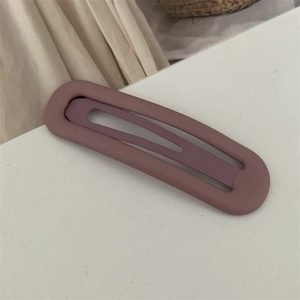 Detail einer matt-violetten hohlen ovalen Haarspange auf einem schlichten weißen Grund