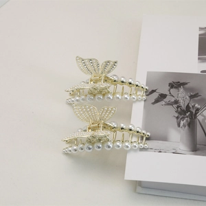 Pinces à cheveux papillon dorées avec perles et strass sur une surface grise épurée