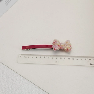 Détail d'une pince à cheveux de 12,5 cm en acétate avec nœud floral et texte doré