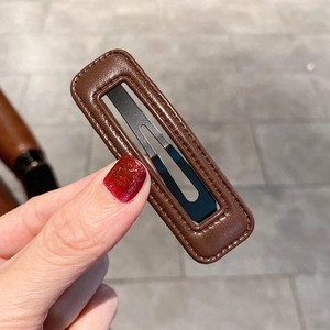 Détail d'une barrette en cuir PU marron avec coutures et attache en métal noir