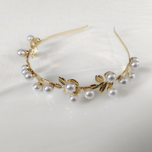 Detail shot of golden metal leaf headband featuring elegant white pearls on white background