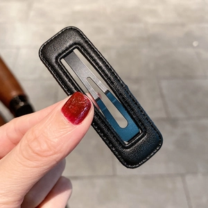 Détail de la barrette BB en cuir noir montrant la texture grainée et les coutures fines