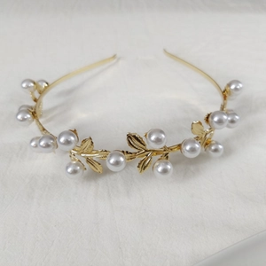 Detailed close-up of golden leaf headband with cream pearls on white textured fabric