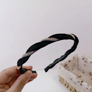Detail showing hand holding a black twisted fabric headband with sparkling silver crystals
