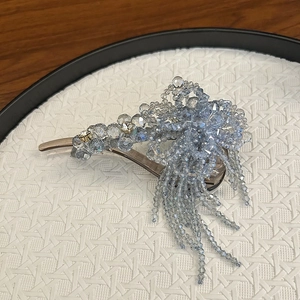Eleganter Blumen-Haarclip mit hellblauen Perlenquasten auf einem weißen gewebten Tablett