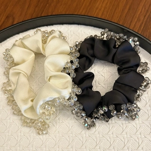 Elegant satin scrunchies with crystal beads in cream and black on a display tray