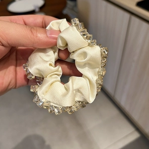 Détail d'un chouchou en satin crème avec des perles de cristal cousues main sur le bord