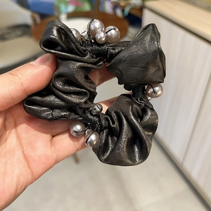 Dettaglio di un elastico in raso nero con perle grigie sintetiche e piccoli sonagli