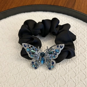 Black velvet hair scrunchie with large crystal butterfly charm on white pedestal